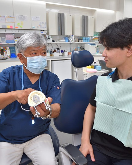 患者に歯の模型を見せて説明する院長